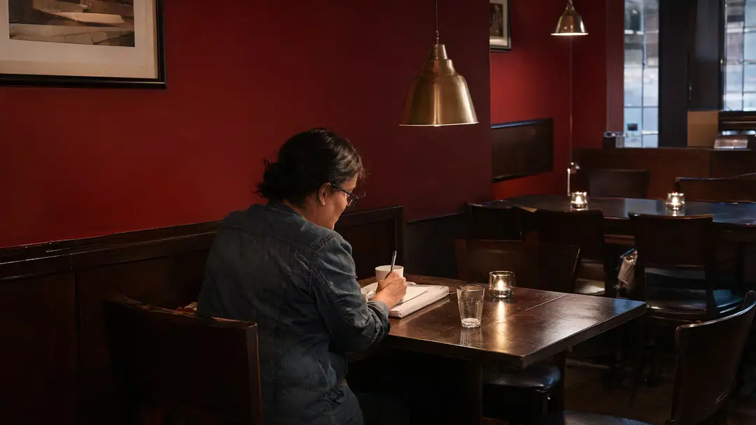 A restaurant owner writing notes at a corner table in her empty dining room after service.