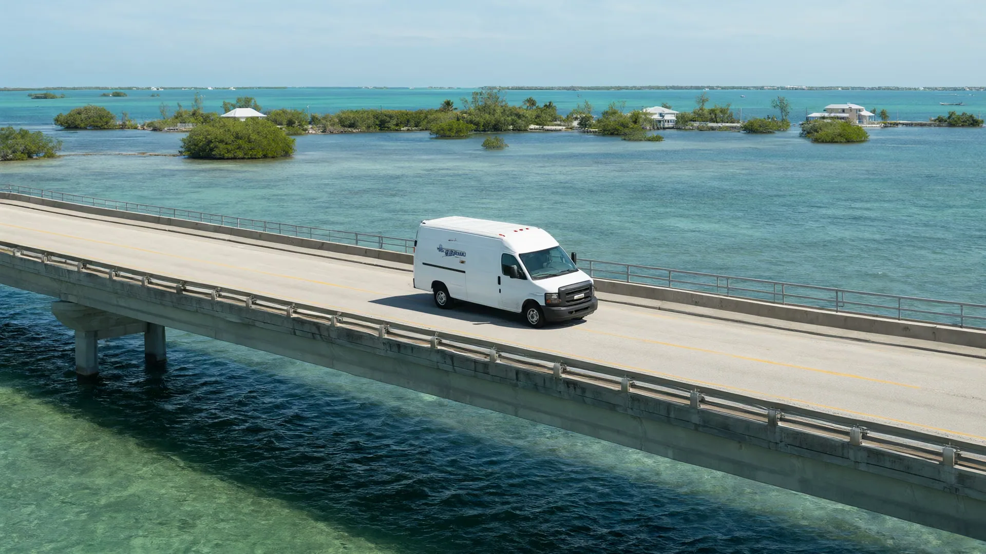 A white work van crossing a long bridge over turquoise water in the Florida Keys.