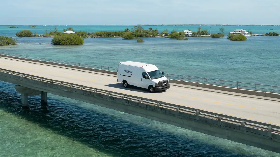 A white work van crossing a long bridge over turquoise water in the Florida Keys.