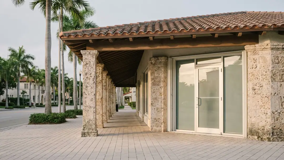 A palm-lined Coral Gables street with a Mediterranean Revival clinic building in soft morning light.