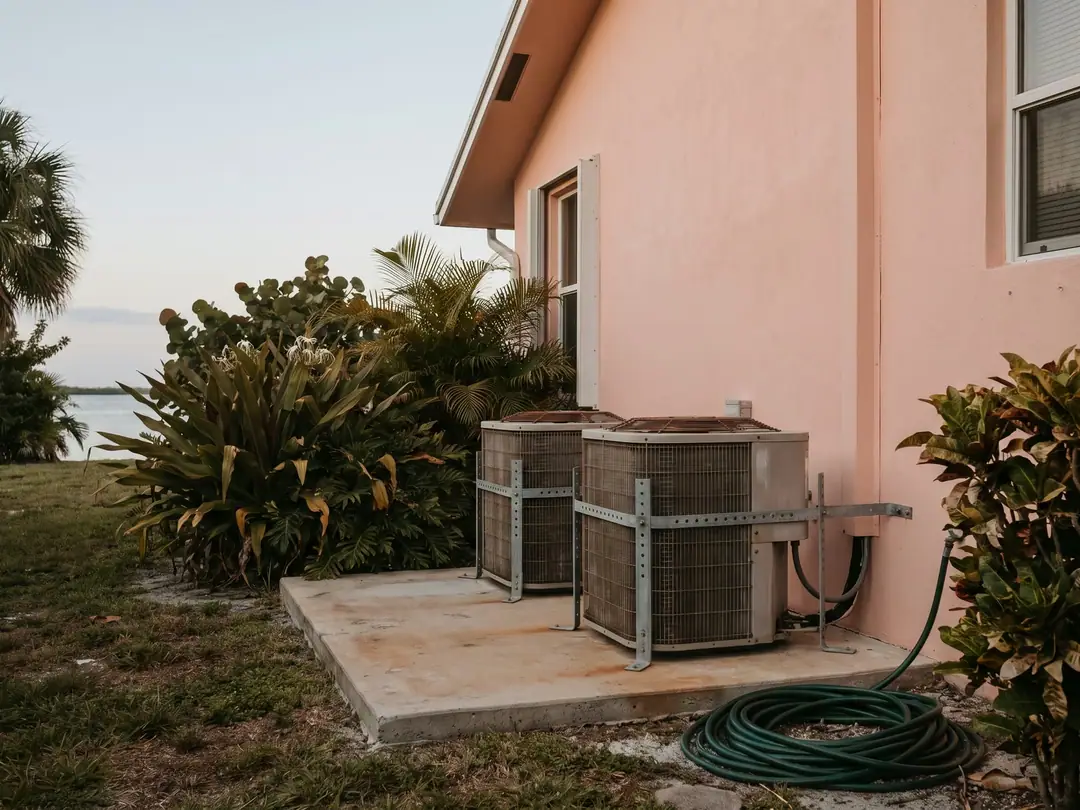 Outdoor heat pump units on a concrete pad beside a stucco home in South Florida.