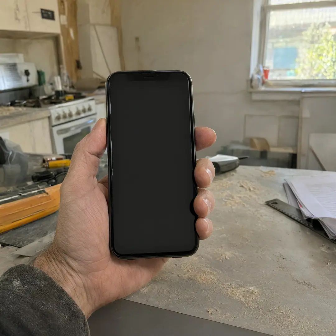 A contractor holds a phone at a kitchen renovation site with tools and sawdust in the background.