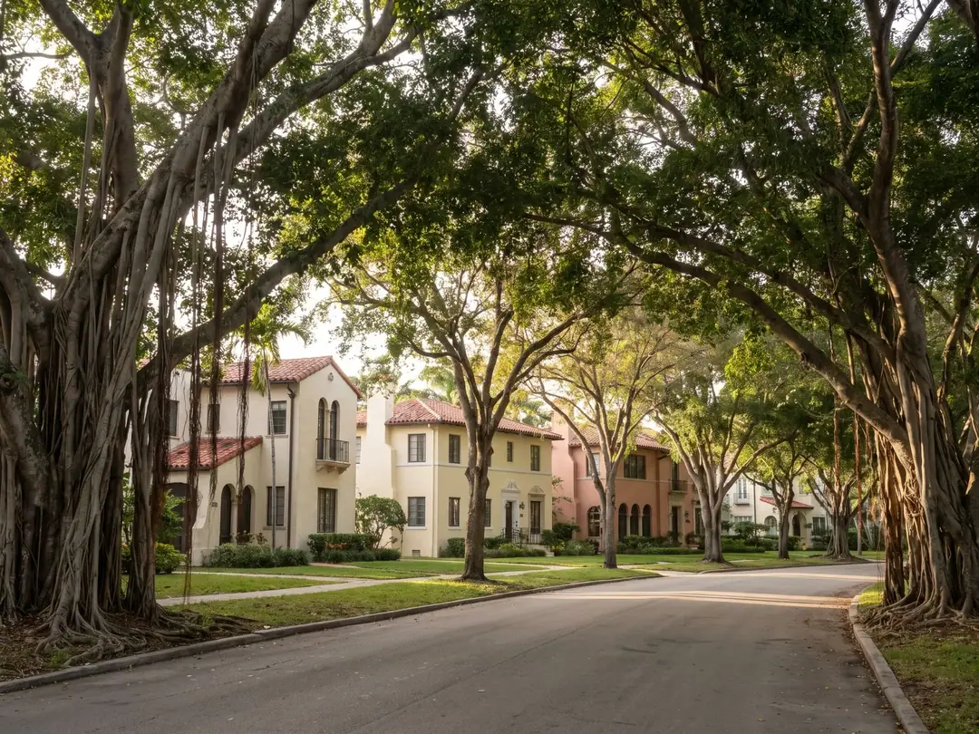 A tree-lined Coral Gables street with Mediterranean Revival homes and banyan trees.