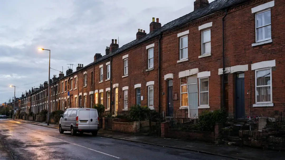Brick terraced houses on a damp Greater Manchester street at dusk with a van parked outside.