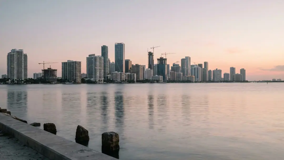 The Brickell skyline at dawn across Biscayne Bay with construction cranes among residential towers.