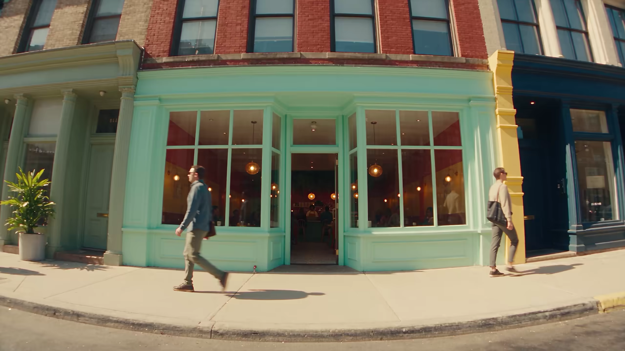 A pastel corner cafe on a sunny street as people walk past